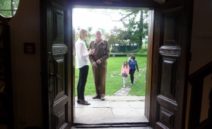 Zdjęcie przedstawia uczestników wydarzenia. W kadrze zdjęcia znajdują się otwarte drzwi, przez które widać ogród i stojących w nim ludzi.