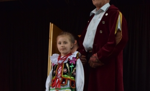 Zdjęcie dwóch uczestników wydarzenia. Starszy mężczyzna i mała dziewczynka stoją na scenie ubrani w tradycyjne stroje.
