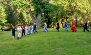 Zdjęcie grupowe uczestników wydarzenia. Uczestnicy przebrani w kostiumy z epoki bawią się dworskim ogrodzie.
