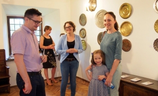 Zdjęcie przedstawia uczestników wystawy. W centrum stoi matka z córką. Po jej lewej stronie kobieta i mężczyzna. Wszyscy są uśmiechnięci. Na ścianie ozdobne tace.