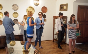 Zdjęcie przedstawia uczestników wystawy. W pomieszczeniu znajdują się cztery kobiety i dwóch mężczyzn. W centrum dwie kobiety rozmawiają, a pozostali oglądają eksponaty.