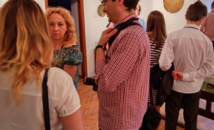 Zdjęcie przedstawia uczestników wystawy. W centrum znajduje się mężczyzna w koszuli, który rozmawia z dwiema kobietami.