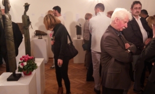 Zdjęcie przedstawia uczestników wystawy. W centrum znajduje się kobieta, która podziwia jedną z rzeźb. Po prawej stronie mężczyzna, który ma założone ręce i kontempluje nad sztuką współczesną.