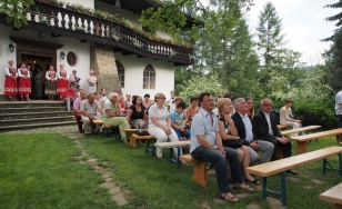 Zdjęcie przedstawia uczestników wydarzenia, którzy siedzą na ławkach przed dworem.