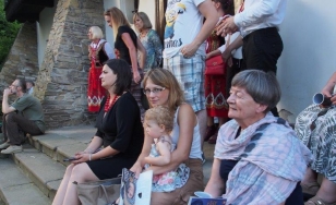 Zdjęcie wykonane od boku przedstawia uczestników wydarzenia. Niektórzy z nich stoją, ale też siedzą na stopniach dworu. Na pierwszy plan wysuwa się zamyślona starsza kobieta z książką w dłoni, a po jej lewej stronie kobieta z dzieckiem.