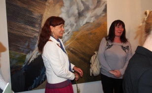 Zdjęcie przedstawia uczestniczki wystawy. Jedna z nich stoi po prawej stronie wielkoformatowego obrazu olejnego.