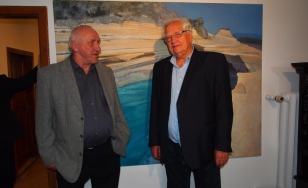 Zdjęcie przedstawia dwóch uczestników wystawy, są to mężczyźni. Stoją oni na tle wielkoformatowego obrazu olejnego Katarzyny Stryszowskiej-Winiarz. Dzieło jest w kolorach niebieskich i jasnobeżowych.