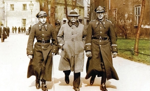Stara fotografia w sepii, przedstawiająca trzech mężczyzn - dwóch z nich to żołnierze w staromodnych mundurach, między nimi idzie starszy mężczyzna z wąsem, ubrany w płaszcz i kapelusz.