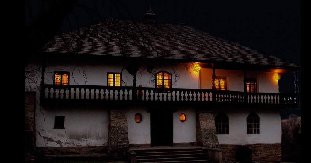 Zdjęcie przedstawiające dwór Stryszów od frontu. Fotografia została wykonana w nocy, niebo za budynkiem jest czarne, wnętrze dworku rozświetlone jest pomarańczowym światłem.