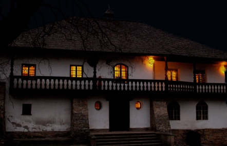 Zdjęcie przedstawiające dwór Stryszów od frontu. Fotografia została wykonana w nocy, niebo za budynkiem jest czarne, wnętrze dworku rozświetlone jest pomarańczowym światłem.