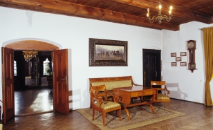 Zdjęcie przedstawia gabinet. Po lewej stronie znajdują się otwarte drzwi. W środkowej części nad zabytkowymi meblami na ścianie wisi obraz.