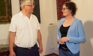 Zdjęcie przedstawia kobietę i mężczyznę, którzy rozmawiają. W tle na ścianach wiszą kolorowe i ozdobne dywany.