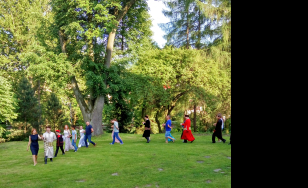 Zdjęcie grupowe uczestników wydarzenia. Uczestnicy przebrani w kostiumy z epoki bawią się dworskim ogrodzie.