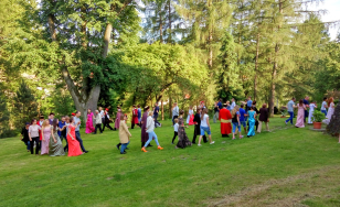 Zdjęcie grupowe uczestników wydarzenia. Uczestnicy przebrani w kostiumy z epoki bawią się dworskim ogrodzie.