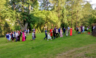 Zdjęcie grupowe uczestników wydarzenia. Uczestnicy przebrani w kostiumy z epoki bawią się dworskim ogrodzie.