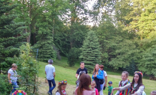 Zdjęcie grupowe uczestników wydarzenia. Uczestnicy przebrani w kostiumy z epoki bawią się dworskim ogrodzie.
